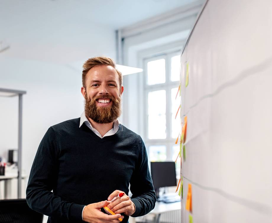 Eignungsabklärung Ein Mann mit rotem Bart steht in einem Büro und hält einen Marker.